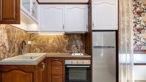 A kitchen with wooden cabinets, a stainless steel refrigerator, a built-in oven, and a marble backsplash. - The Owl House (Chania)