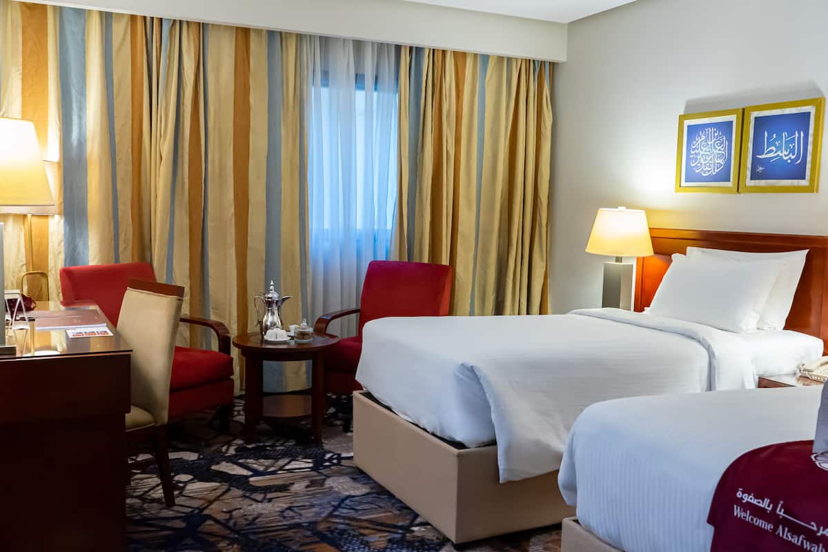 Habitación de hotel con cama, dos sillas, escritorio, televisor y ventana con cortinas.