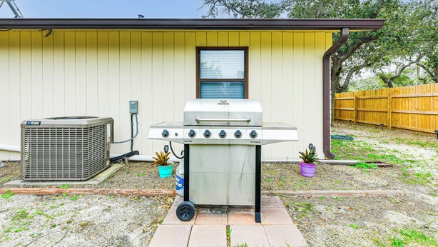 Een draagbare grill in een achtertuin, met een geel huis, een schotelantenne en een houten omheining.