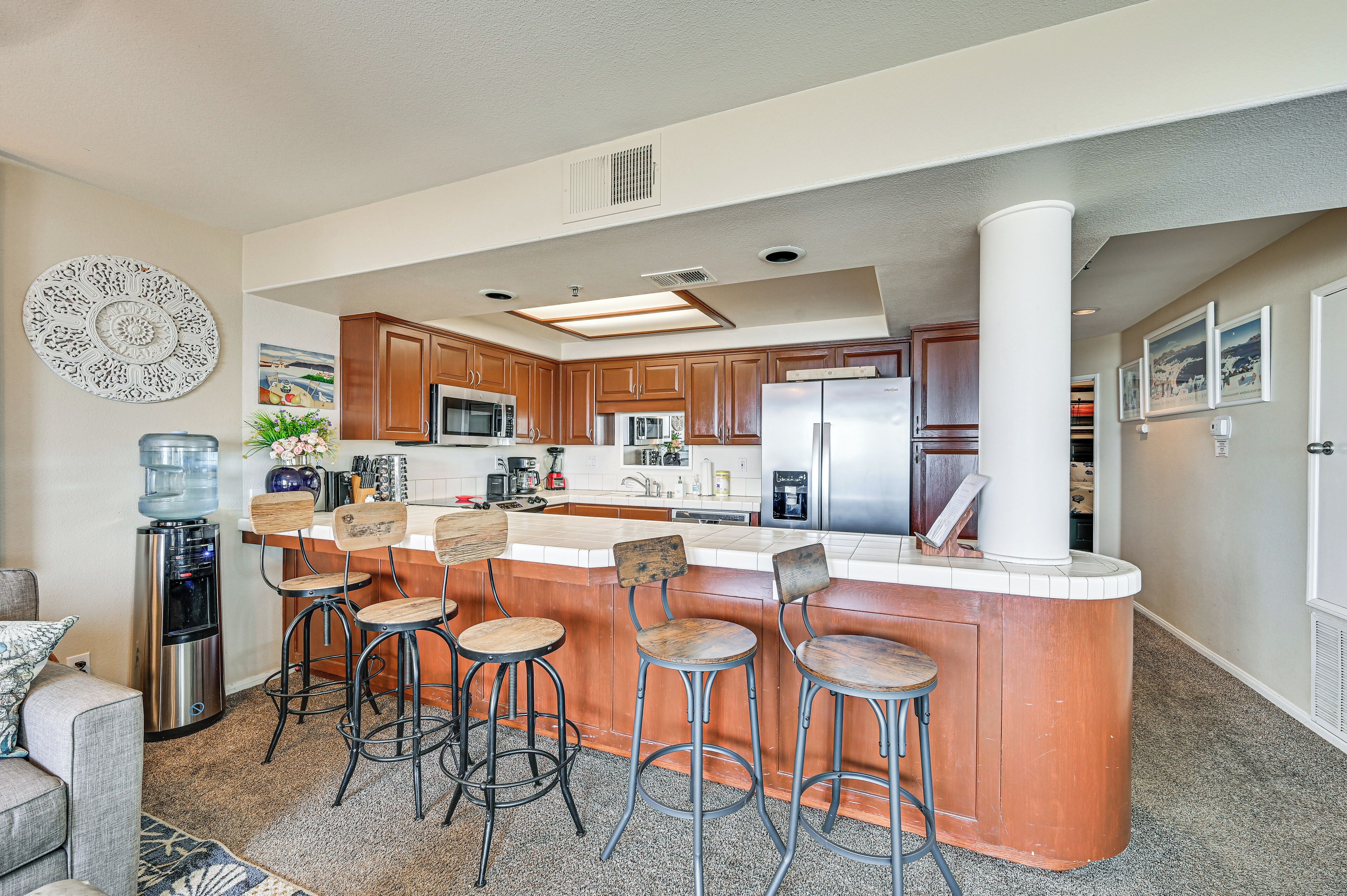 A modern kitchen with a central island, bar stools, stainless steel appliances, and a water dispenser.