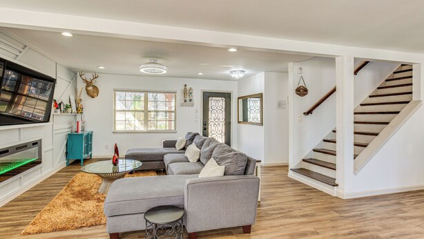 A modern living room with a sectional sofa, a glass coffee table, and a fireplace. There is a staircase to the right and a view of the outside through a window. - Waterfront Retreat w/ Dock on Lake Tawakoni! (Quinlan)