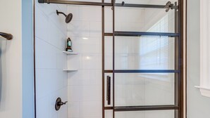 A modern shower enclosure with a glass door, a towel rack, and a shelf with toiletries. - Cozy North Carolina Retreat Near Fishing & Boating (Washington)
