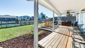 En overdækket udendørs terrasse med trægulv, metalstole og et siddeområde med et bord og stole.