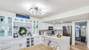 A modern kitchen with white cabinetry, a wooden dining table, and a stainless steel refrigerator. - Regatta Bay Condo w/ Balcony + Water Views! (Lake Ozark)
