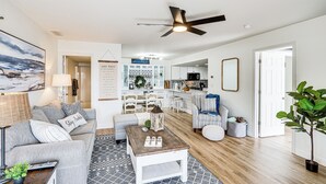 A modern living room with a grey sofa, a coffee table, and a dining area with a kitchen in the background. - Regatta Bay Condo w/ Balcony + Water Views! (Lake Ozark)