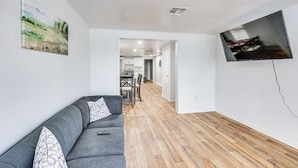A modern living room with a grey sofa, a flat-screen TV mounted on the wall, and a wooden floor. - Charming El Dorado Retreat Near Main Street! (El Dorado)