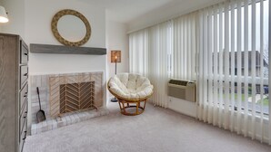 Una sala moderna con chimenea, un ventanal con persianas, un sillón de mimbre y un espejo redondo en la pared.