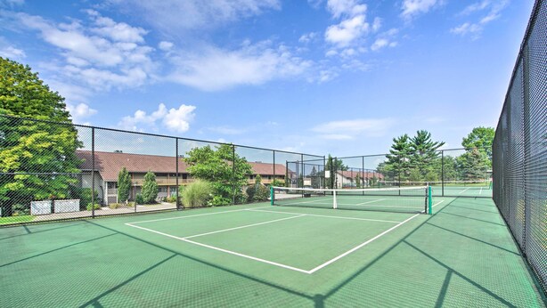 Cancha de tenis al aire libre con red, rodeada por una cerca de malla y árboles.
