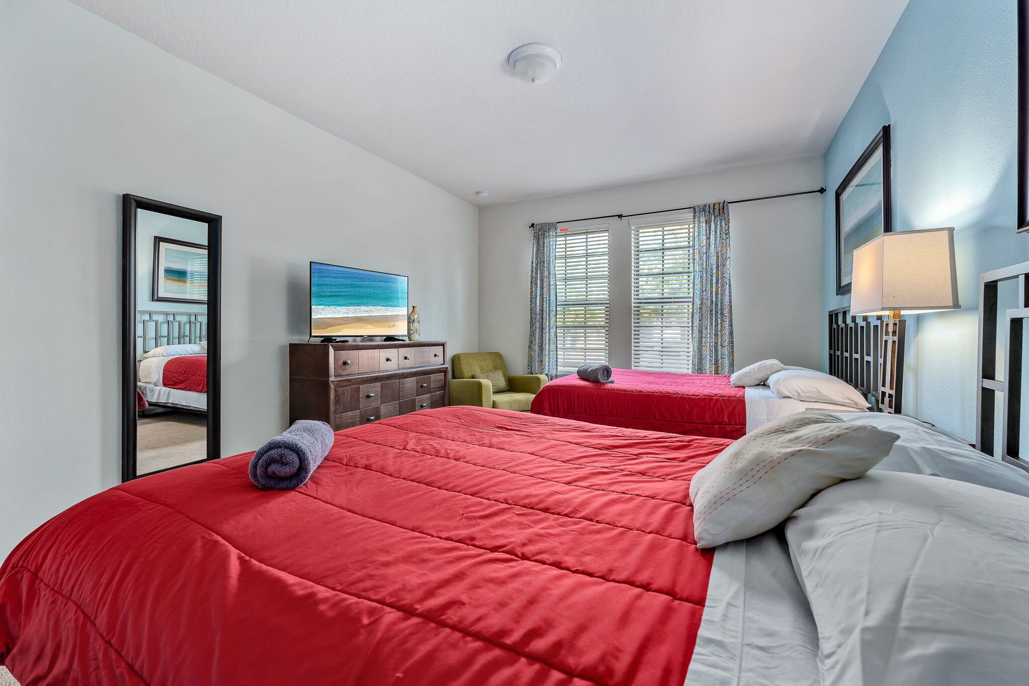 A hotel room with two beds, a TV, a dresser, a chair, and a window with curtains.