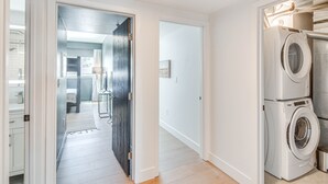 A laundry area with stacked washing machines and a dark wooden door leading to a bathroom. - Downtown Winter Park Condo w/ Free Bus to Ski Base (Winter Park)