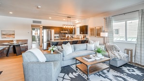 A modern living room with a sofa, coffee table, and a dining area with a bench. - Downtown Winter Park Condo w/ Free Bus to Ski Base (Winter Park)
