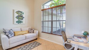 A living room with a sofa, a dining table with a chair, a window with blinds, and a fish illustration on the wall. - Cozy Cape Coral Home: 8 Mi to Marina! (Cape Coral)