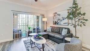 A modern living room with a sectional sofa, a coffee table, patterned chairs, a potted plant, and a painting on the wall.