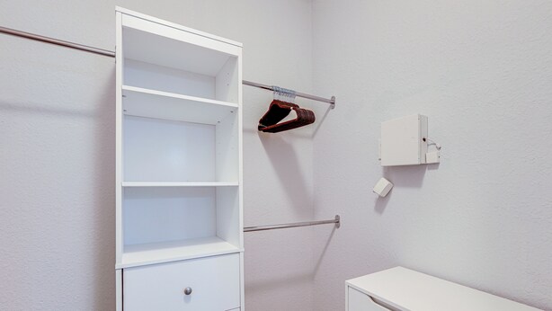 A white closet with open shelves, a hanging rack, and a small white cabinet.