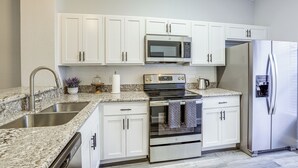 A kitchen with white cabinets, stainless steel appliances, granite countertops, and a built-in dishwasher.