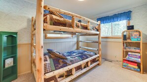 Un lit superposé avec une couvre-lit matelassée, une bibliothèque remplie de jeux de société et une fenêtre donnant sur les arbres.