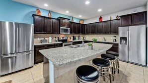 Una cocina moderna con armarios de madera oscura, electrodomésticos de acero inoxidable, encimera de granito y una isla central con taburetes de bar.