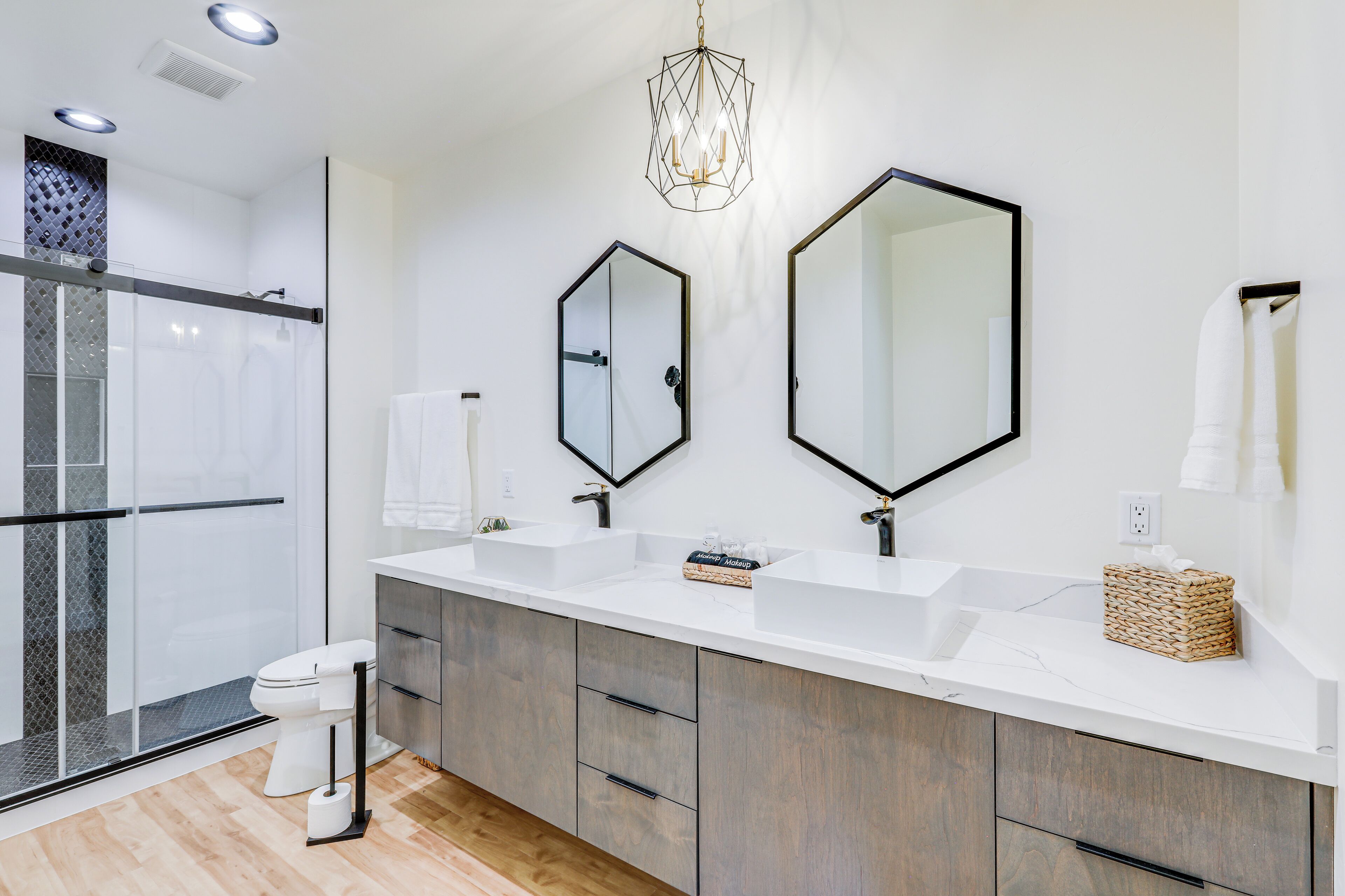 A modern bathroom with a glass shower enclosure, a white toilet, two sinks, and a large mirror.