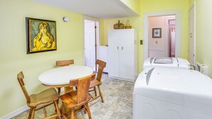 Una habitación con una mesa de comedor y sillas, una lavadora blanca, un armario blanco y un cuadro en la pared.