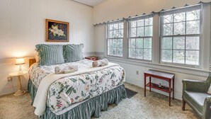 Un dormitorio con cama, mesita de noche, silla, ventana con vistas y un cuadro en la pared.