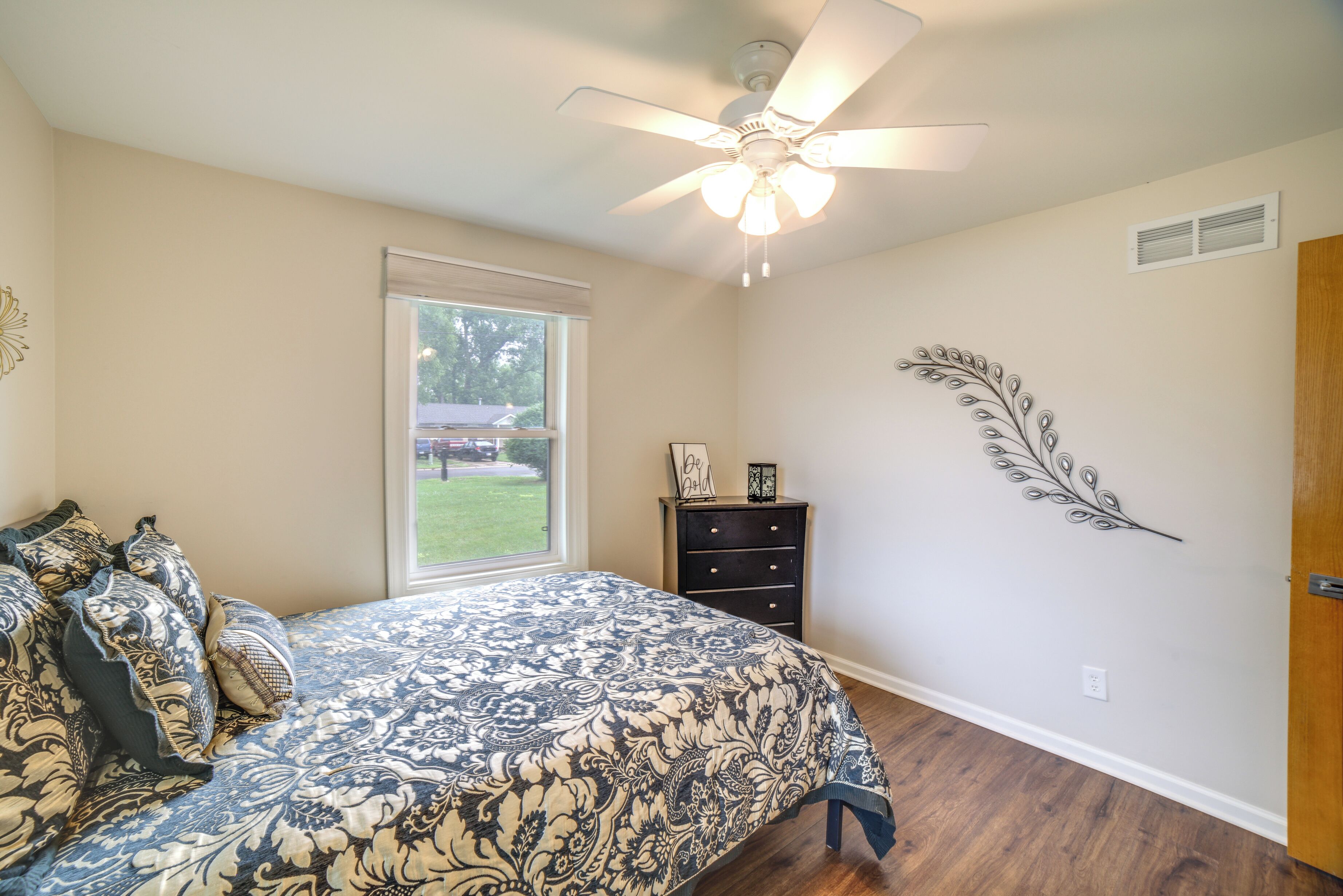 A bedroom with a bed, a ceiling fan, a window, a dresser, and wall art.