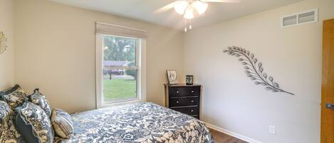 A bedroom with a bed, a ceiling fan, a window, a dresser, and wall art.