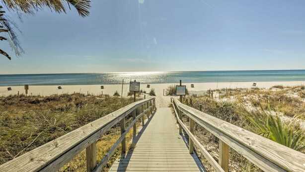 A wooden boardwalk leading to a beach with a clear sky and calm sea. - Walk to Beach: PCB Condo w/ Oceanfront Pool Access (Panama City Beach)