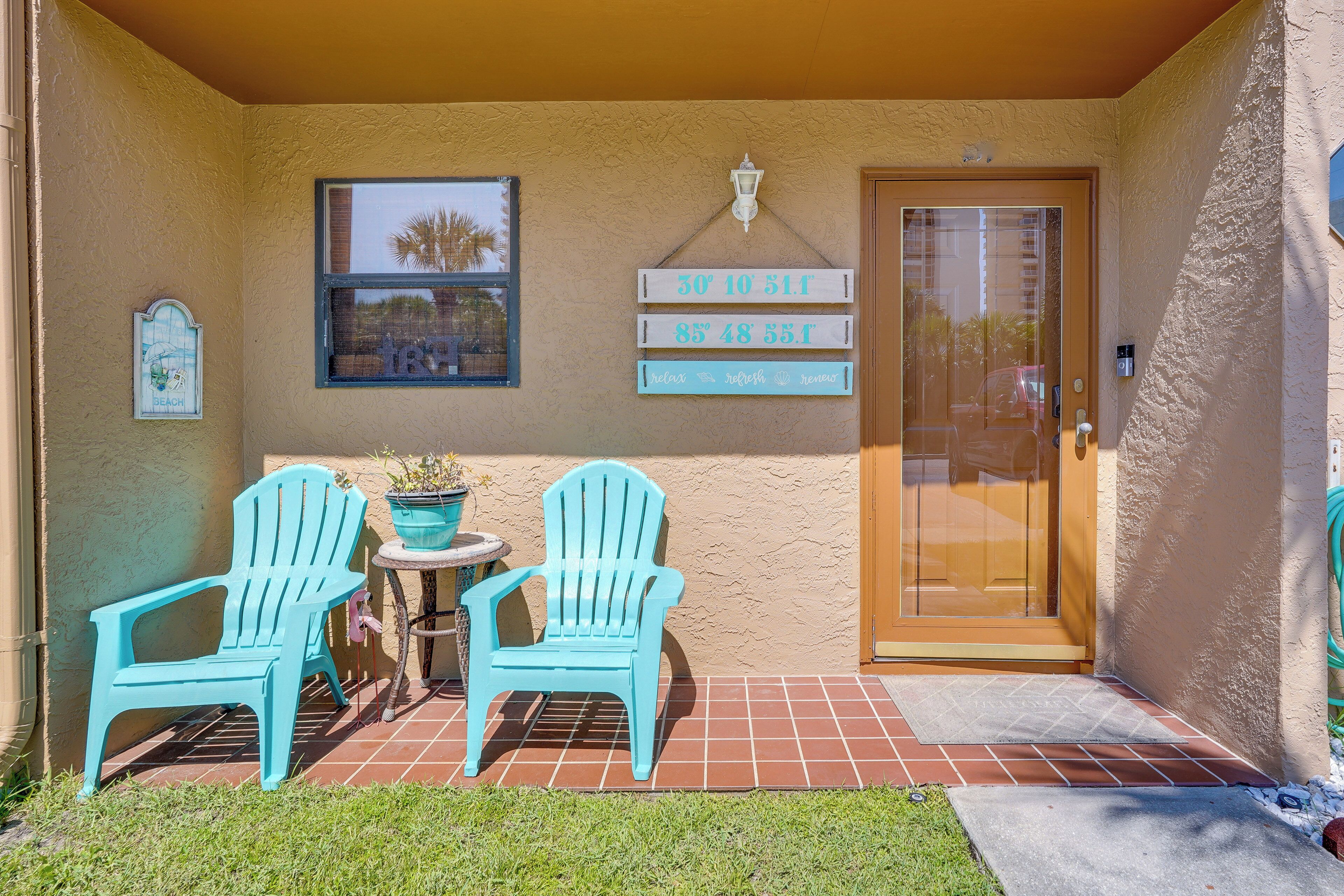 A covered patio with two turquoise Adirondack chairs, a small table, and a potted plant. There are signs on the wall indicating a beach and a refreshment area.
