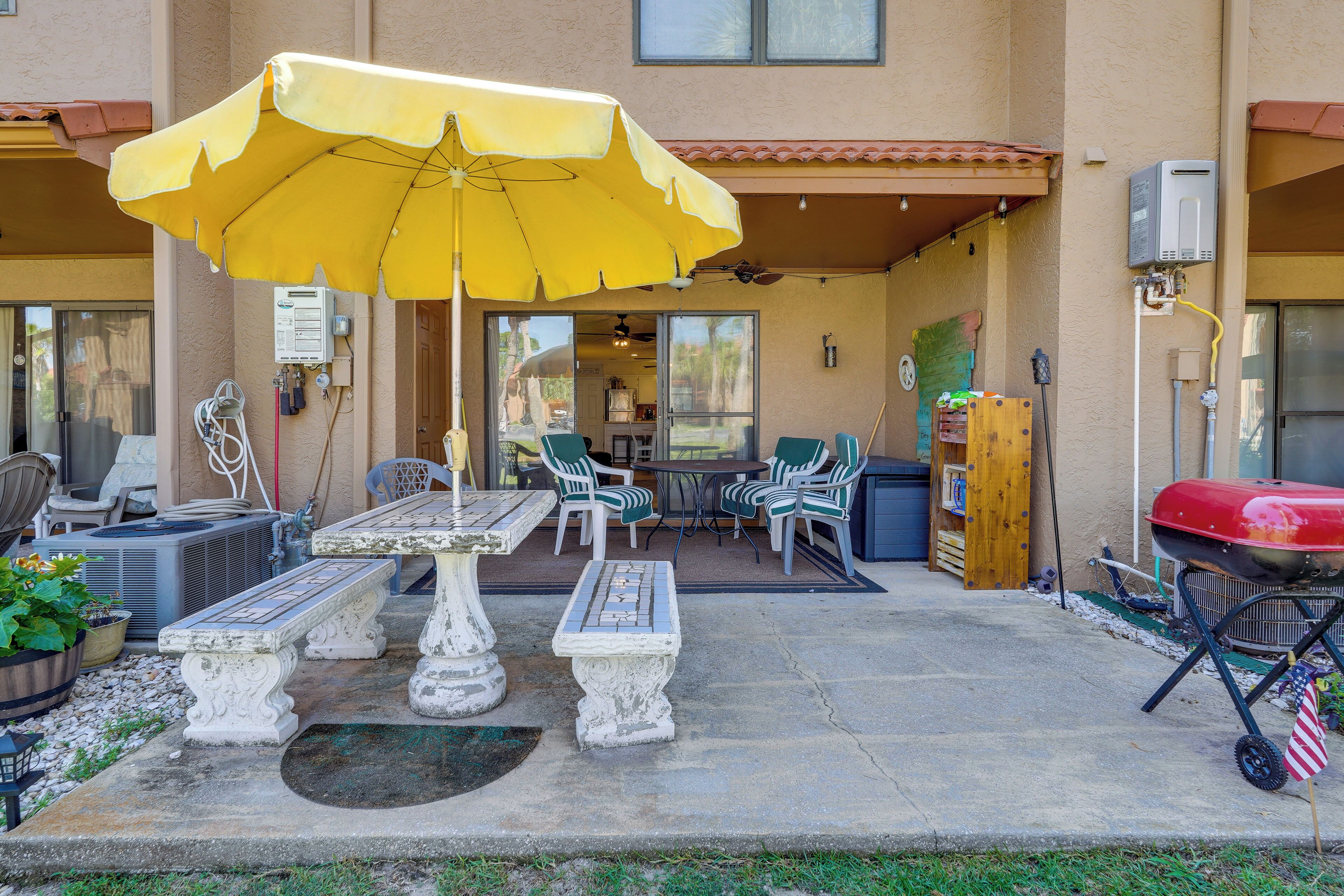 Eine Terrasse im Freien mit einem gelben Sonnenschirm, Gartenmöbeln und einem Grill.