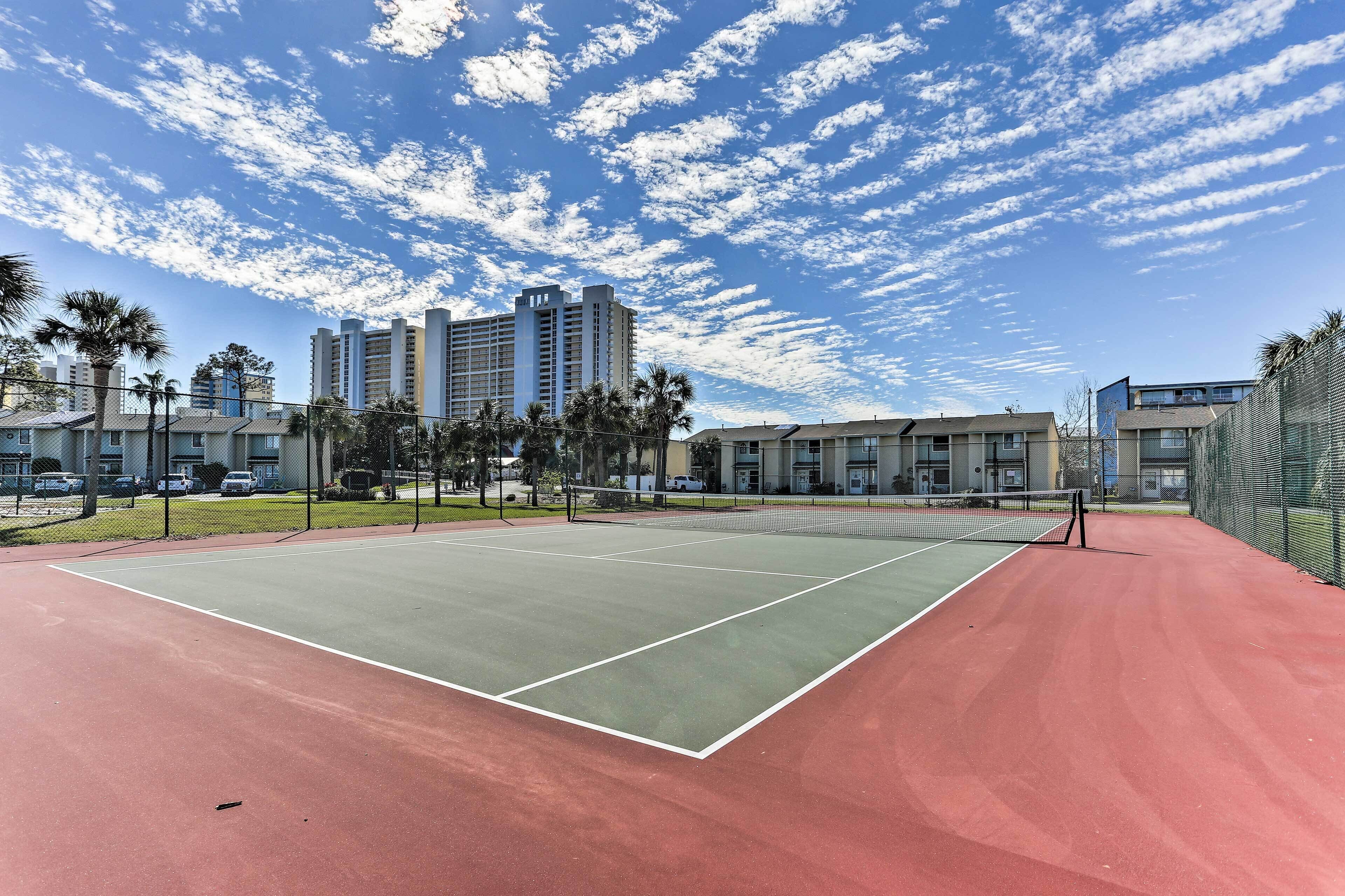 Una cancha de tenis con red, rodeada de una valla y palmeras.