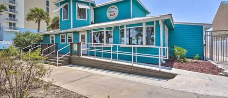 Een turquoise gebouw met een bord waarop 'Coco Beach Inn' staat. Het heeft een overdekte veranda met treden die naar de ingang leiden.