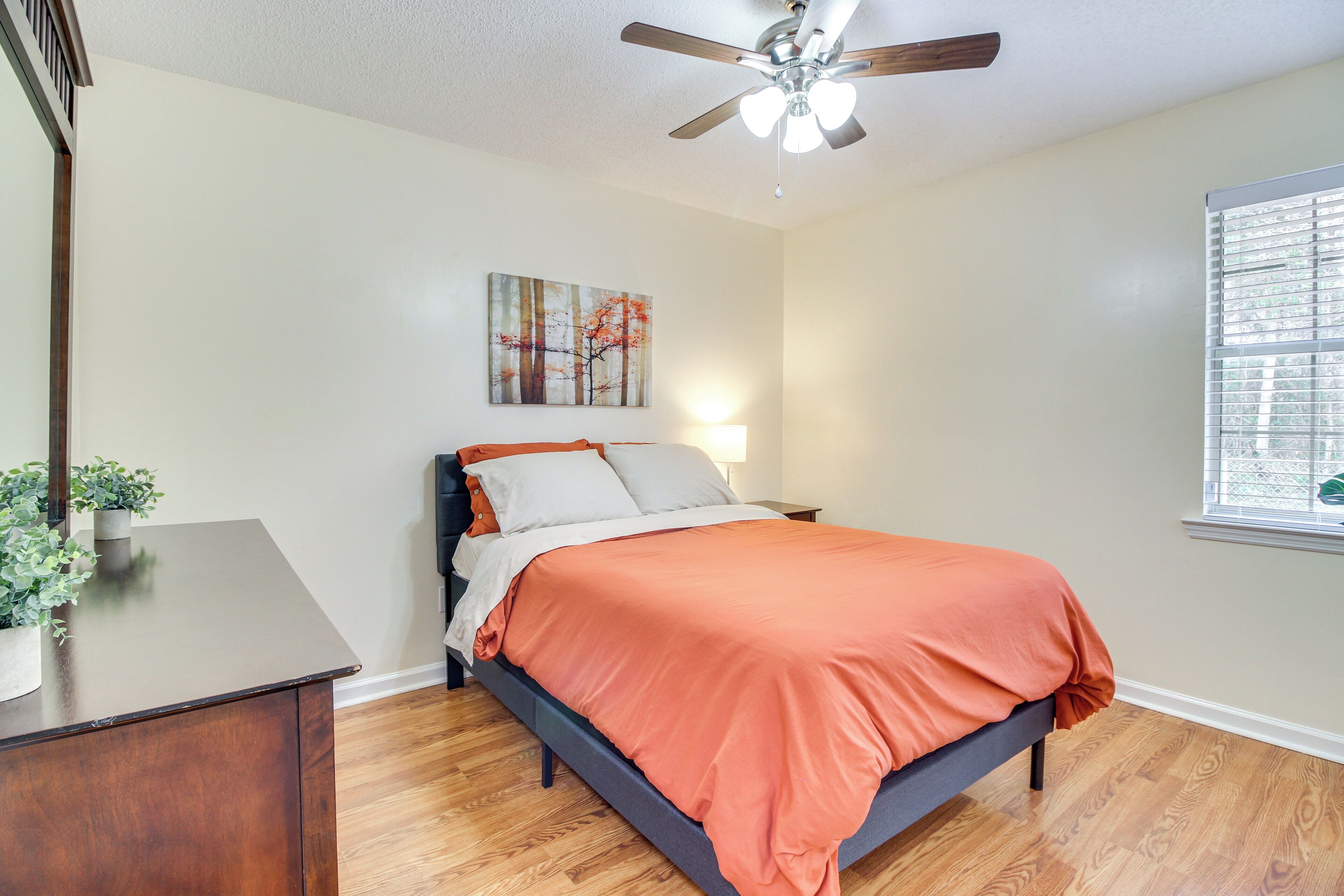 Une chambre à coucher avec un lit, un ventilateur de plafond, une fenêtre avec des stores et un tableau au mur.