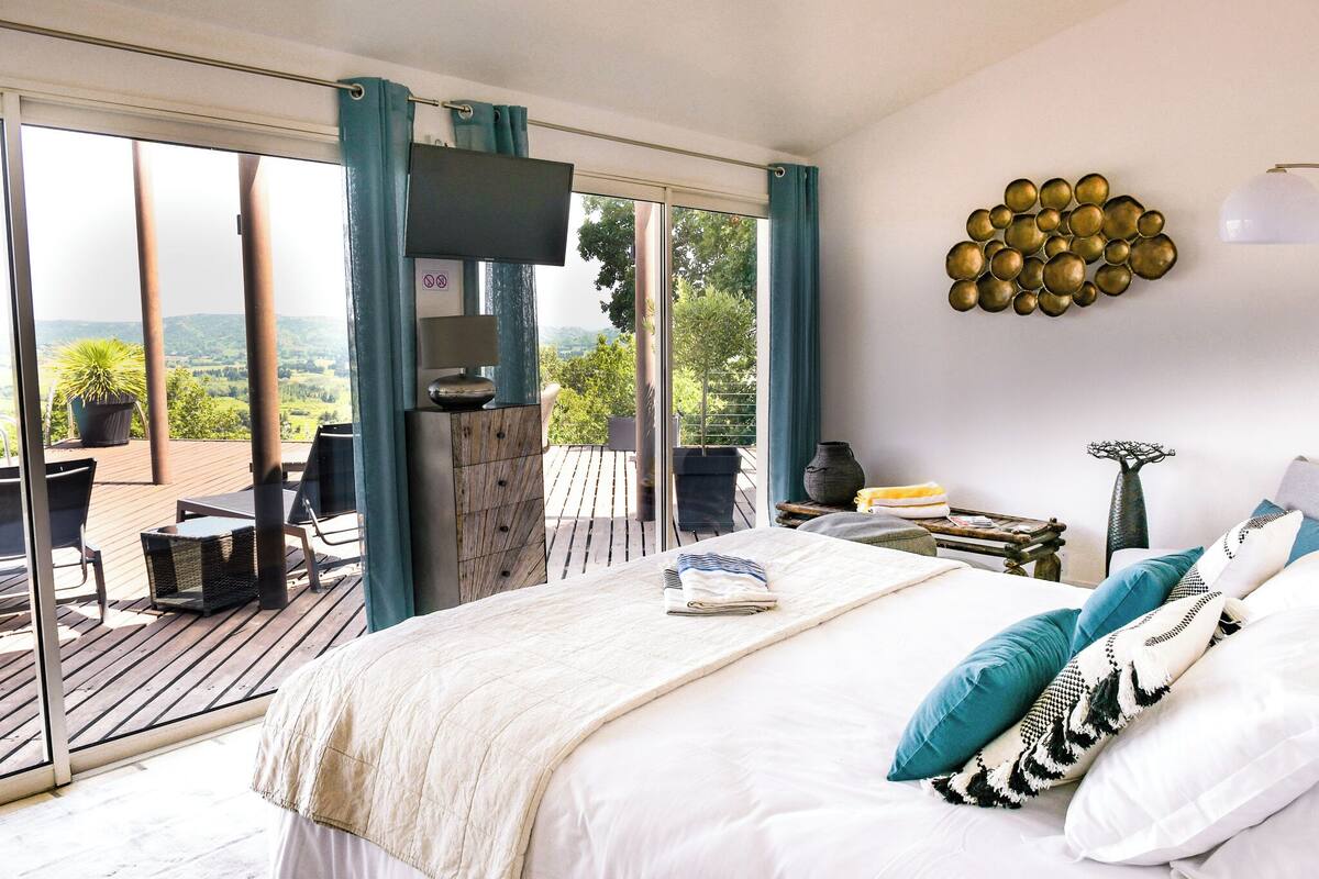 Een slaapkamer met een groot bed, uitzicht op de natuur en een balkon met meubels.