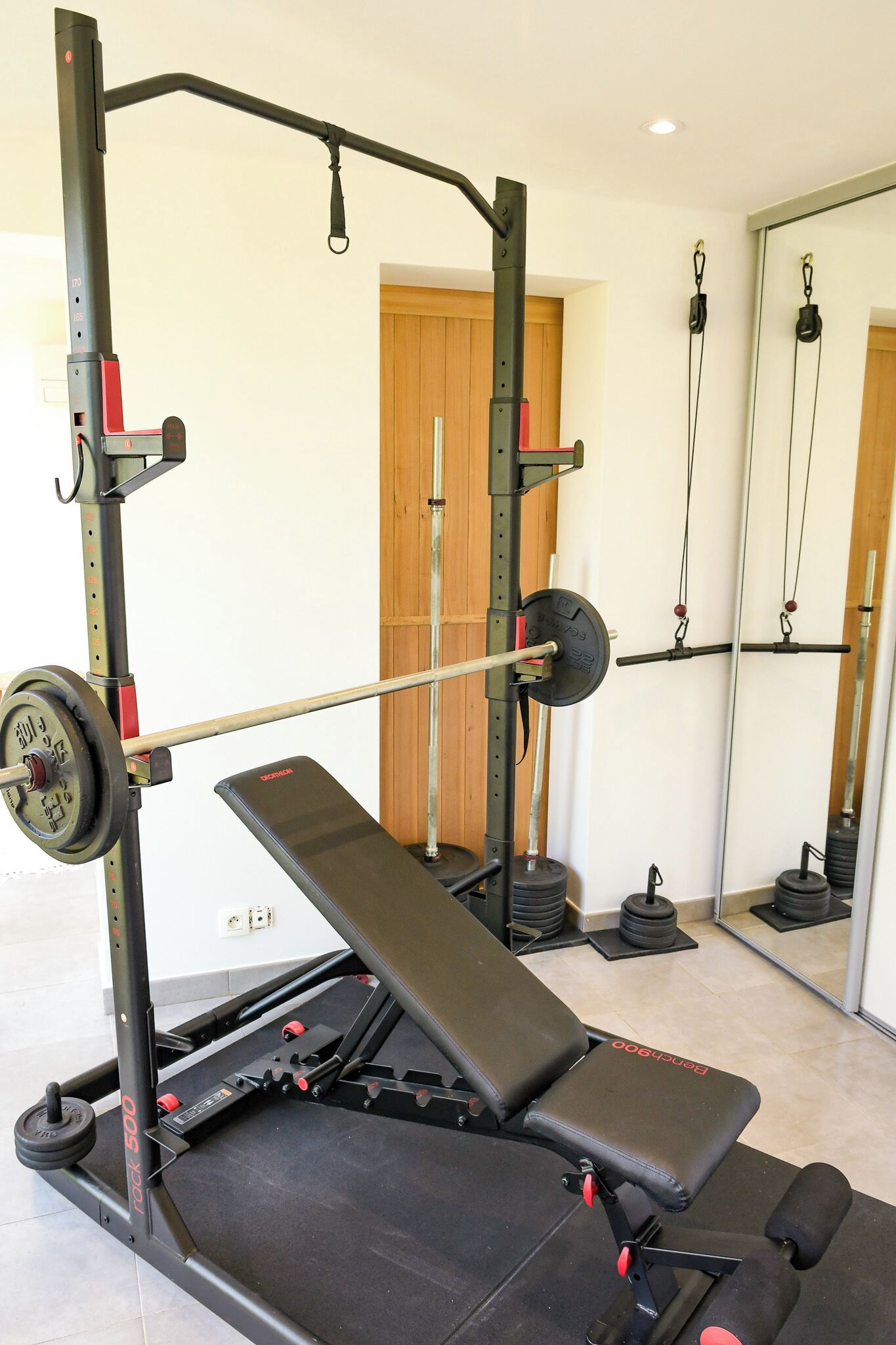 A gym with a bench press, weight rack, and mirrors.
