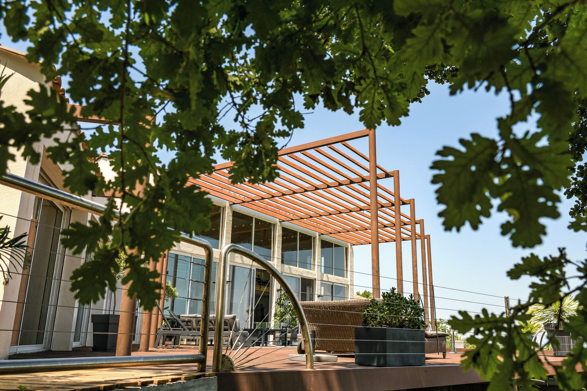 Um edifício moderno com grandes janelas, área externa coberta com assentos e uma estrutura de pérgola.