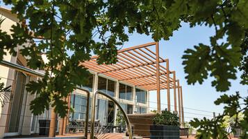 Um edifício moderno com grandes janelas, área externa coberta com assentos e uma estrutura de pérgola.