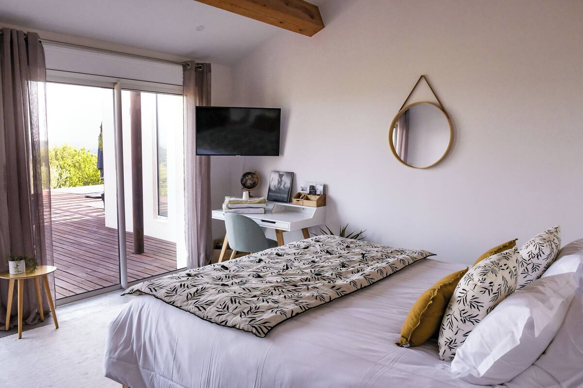 Een slaapkamer met een bed, een bureau, een televisie en uitzicht door een schuifdeur.