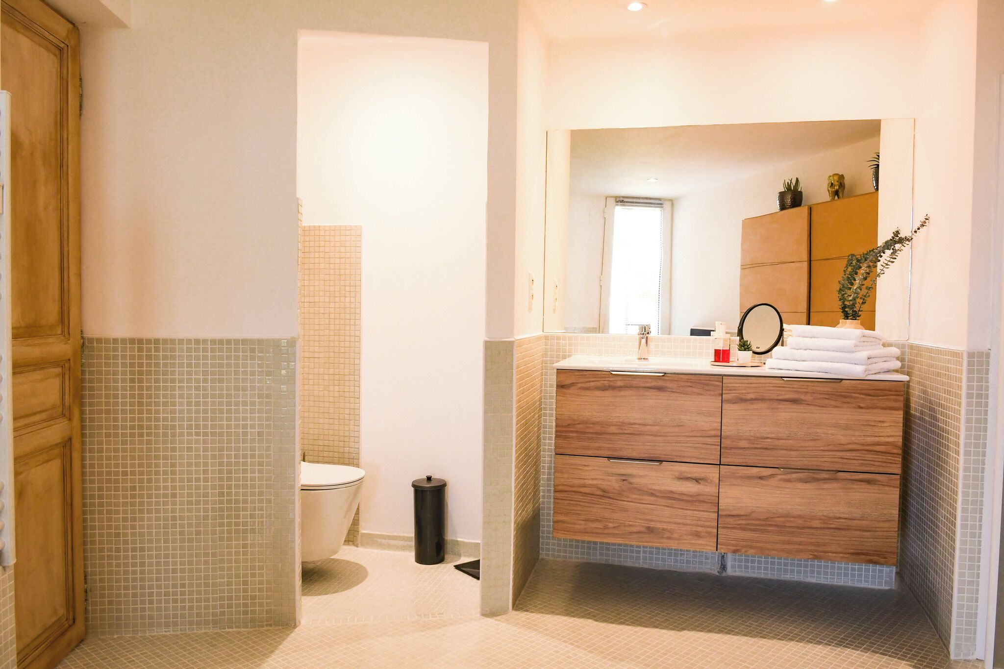 Un baño moderno con tocador de madera, un espejo y zona de ducha con azulejos.