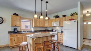 Una cocina con armarios de madera, encimera de granito, refrigerador blanco y tres taburetes de madera.