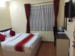A hotel room with a bed, a desk, a television, and a window with curtains. - Hotel Odyssey Nepal (Kathmandu)