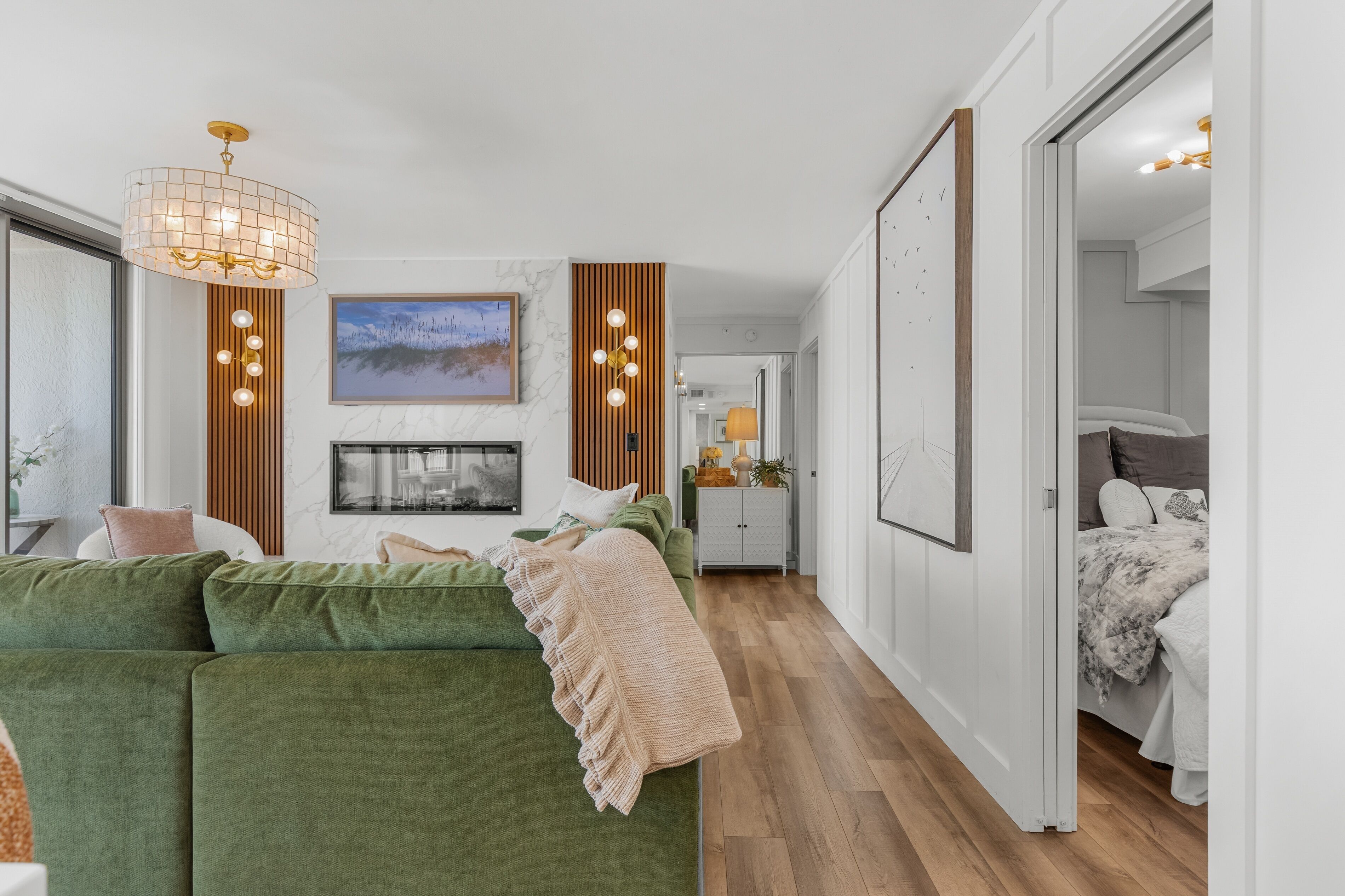 A modern bedroom with a green sofa, a bed with a patterned duvet, a wooden floor, and a hallway leading to another room.
