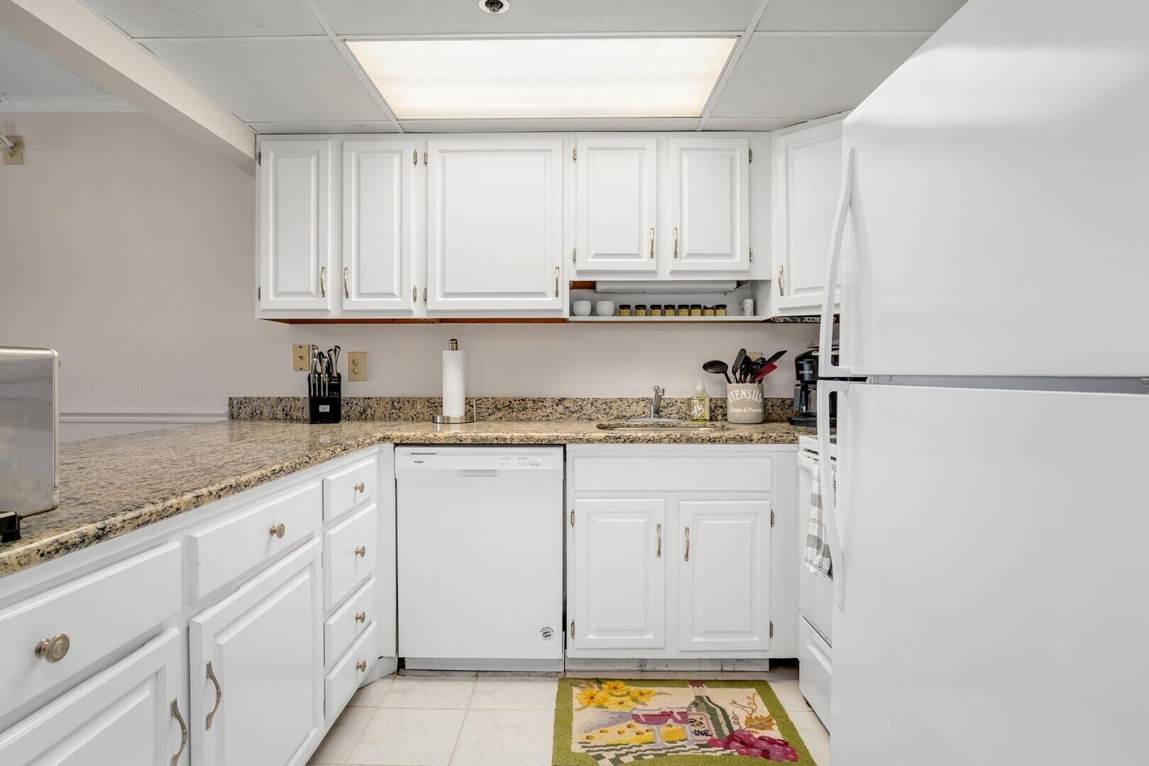A kitchen with white cabinets, a granite countertop, a dishwasher, and a refrigerator.