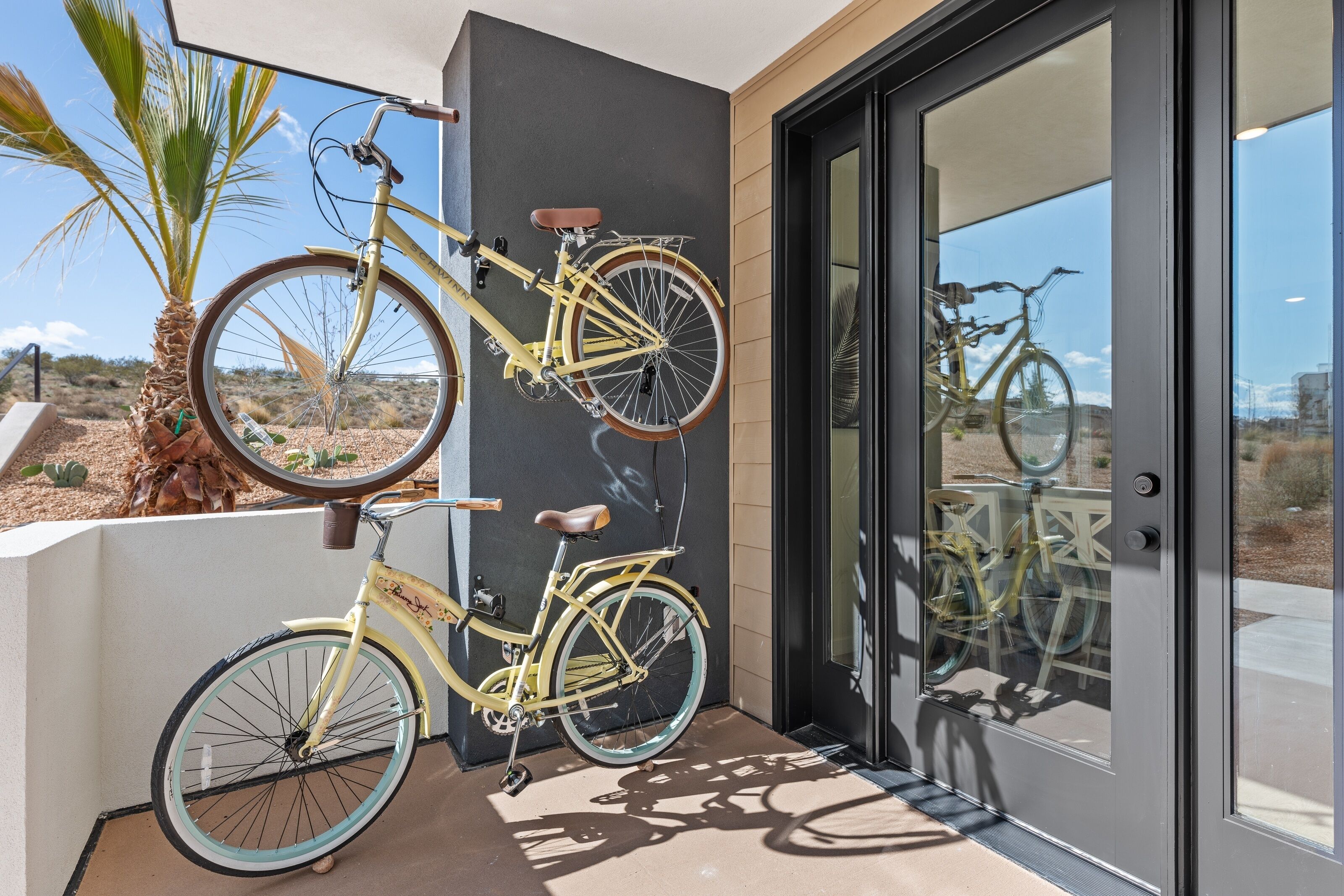 Una bicicleta amarilla estacionada en un balcón con vistas a un paisaje desértico y una palmera.
