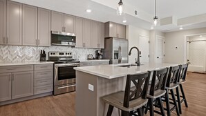 A modern kitchen with stainless steel appliances, a large island with bar stools, and a herringbone-patterned backsplash.