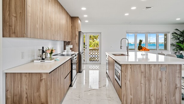 A modern kitchen with wooden cabinets, a marble countertop, and a view of the sea through large windows. - Luxury condo with stunning intracoastal water views, near downtown West Palm Bch (West Palm Beach)