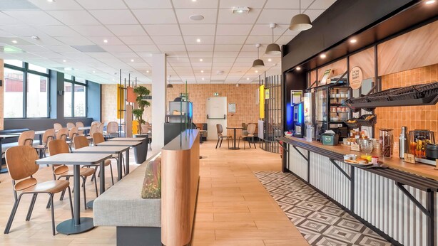 Een modern café met een lange toonbank, een zithoek en een keuken die zichtbaar is door de glazen wand.