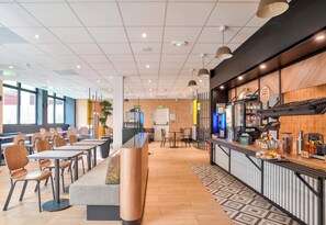 Un café moderne avec un long comptoir, un espace salon et une cuisine visible à travers un mur de verre.