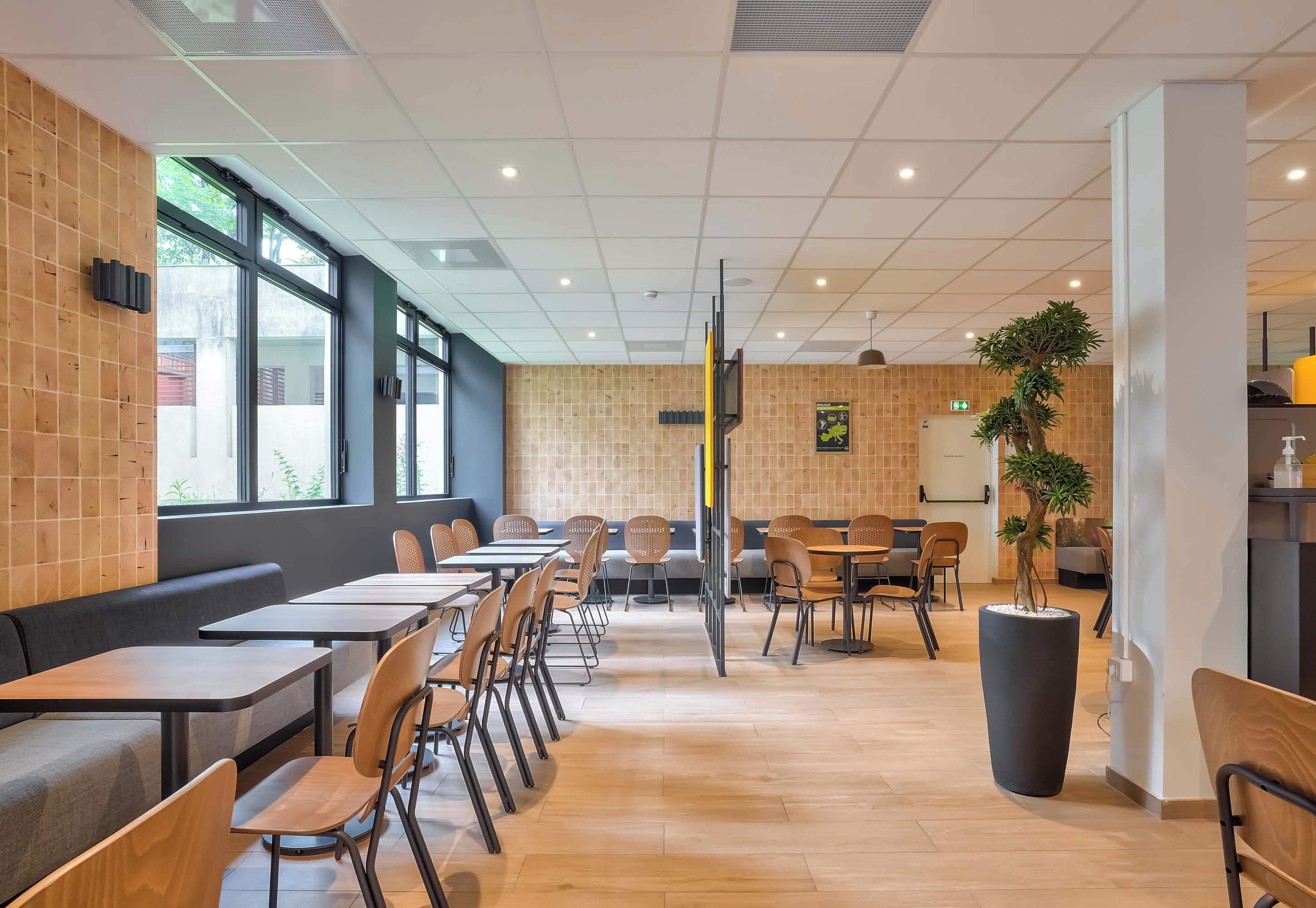 A modern restaurant with wooden flooring, black and wooden chairs, and tables.