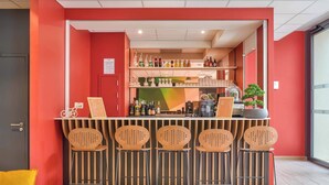 Een bar met een rode muur, verschillende flessenrekken en vijf barstoelen.