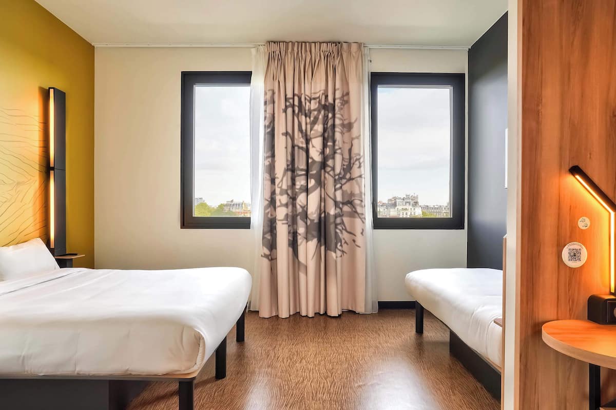 Hotellihuone, jossa on kaksi sänkyä, suuri ikkuna ja puukuviollinen verho.
